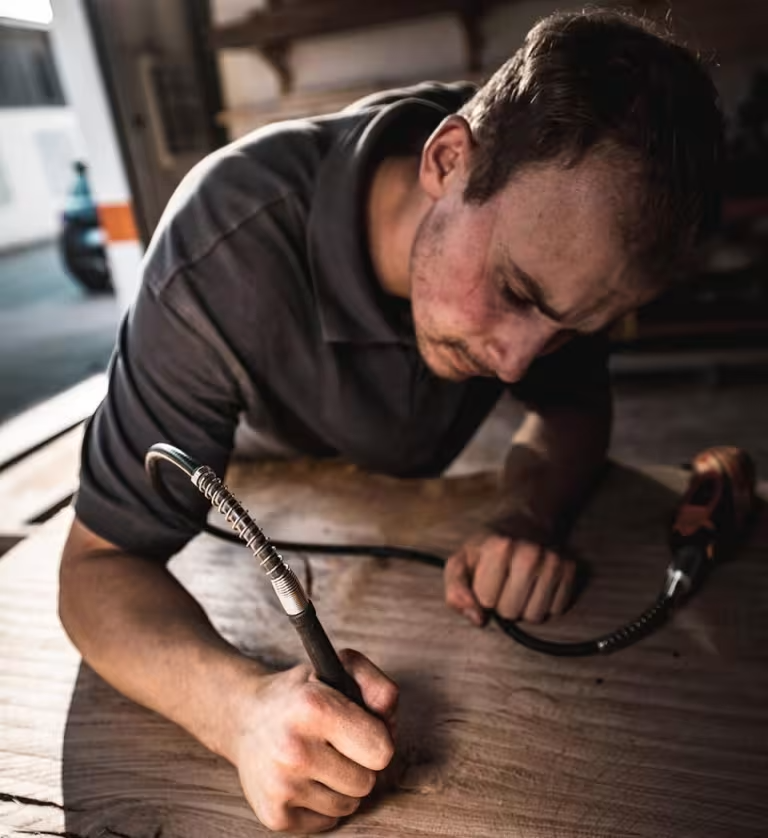 Dominik Becker arbeitet konzentriert an einer massiven Holzbohle